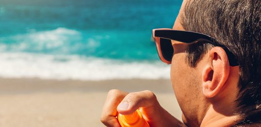 Sun cream protection. Man sprays sun cream on his shoulder. Skin care concept. Healthy skin on vacation.